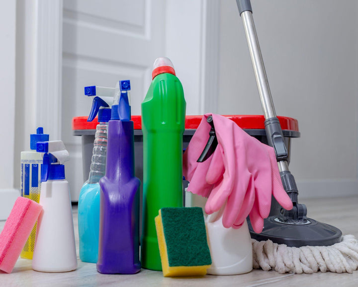 Sprayflacons, een mop, een emmer en rubberen handschoenen op een witte vloer