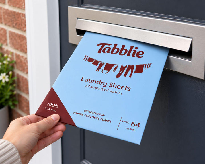 Een hand houdt een pak Tabblie Wasstrips voor de brievenbusklep van een voordeur