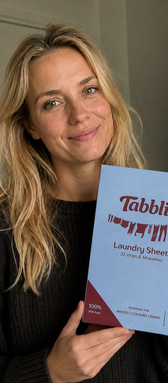 Vrouw houdt een pak Tabblie wasstrips vast en lacht in de camera