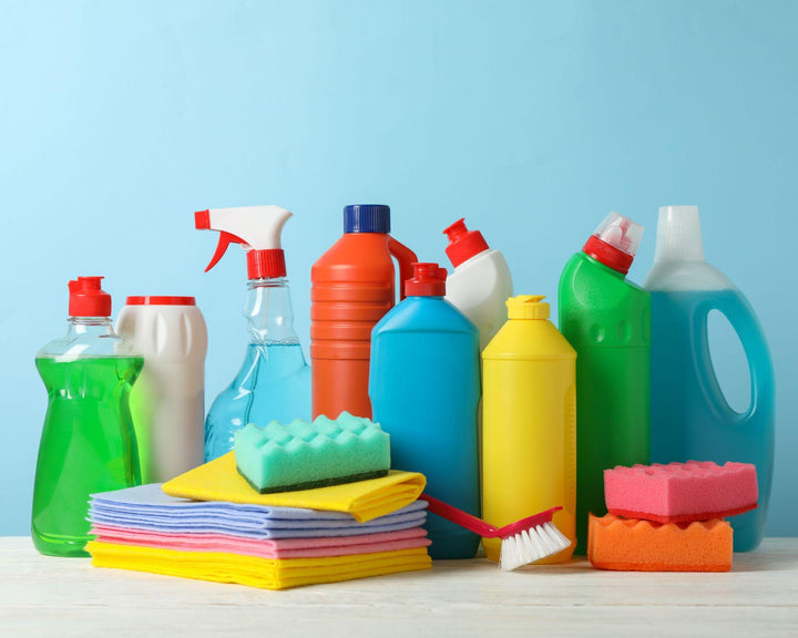 Verzameling kleurrijke schoonmaakmiddelen, flessen, doekjes en sponzen op een lichtblauwe achtergrond