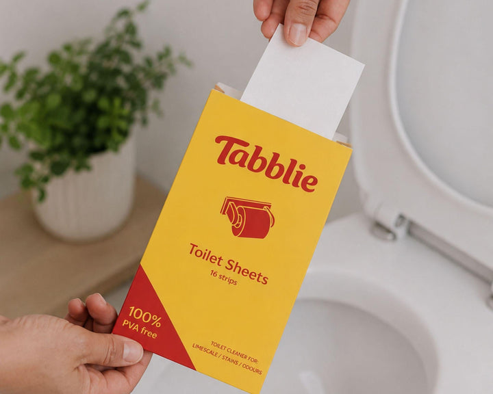 Een hand houdt een pak Tabblie Toiletstrips boven de toiletpot