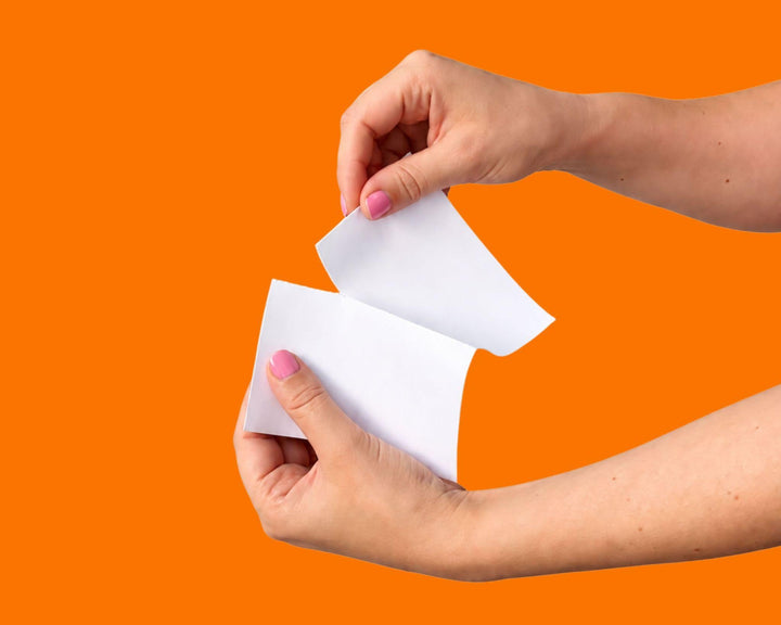 Twee handen scheuren een Tabblie wasstrip doormidden op een oranje achtergrond